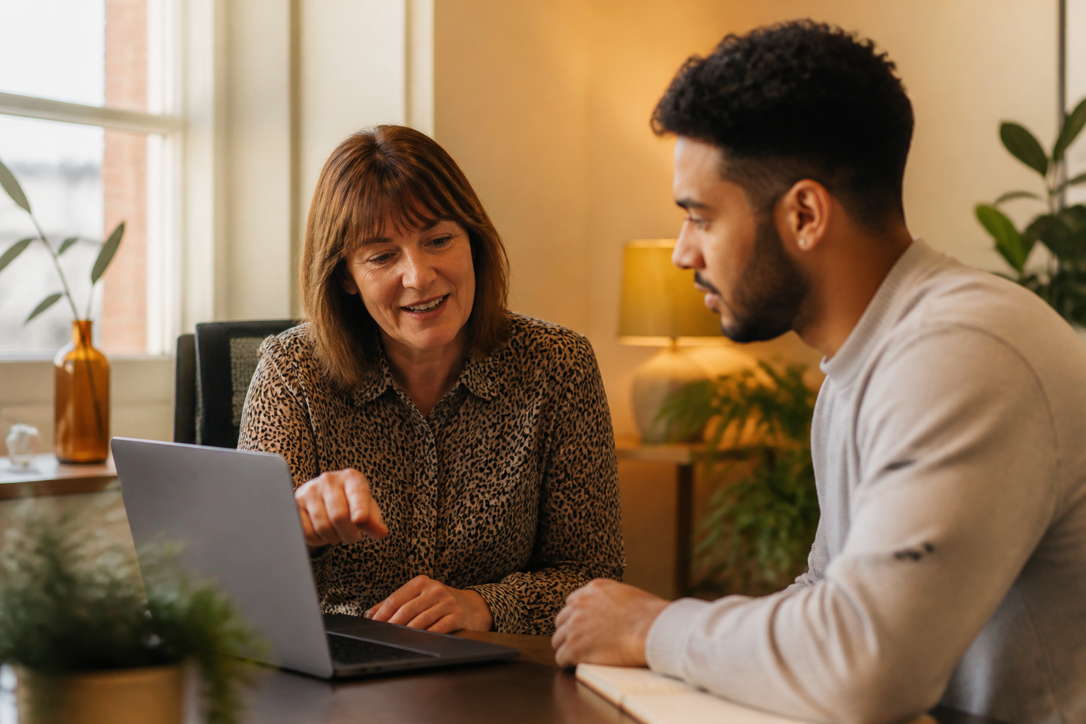 An HR lead discussing employee benefits with a colleague at an office desk.
