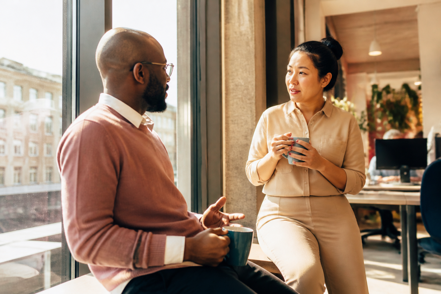 Two colleagues discussing workplace green benefits by a bright window