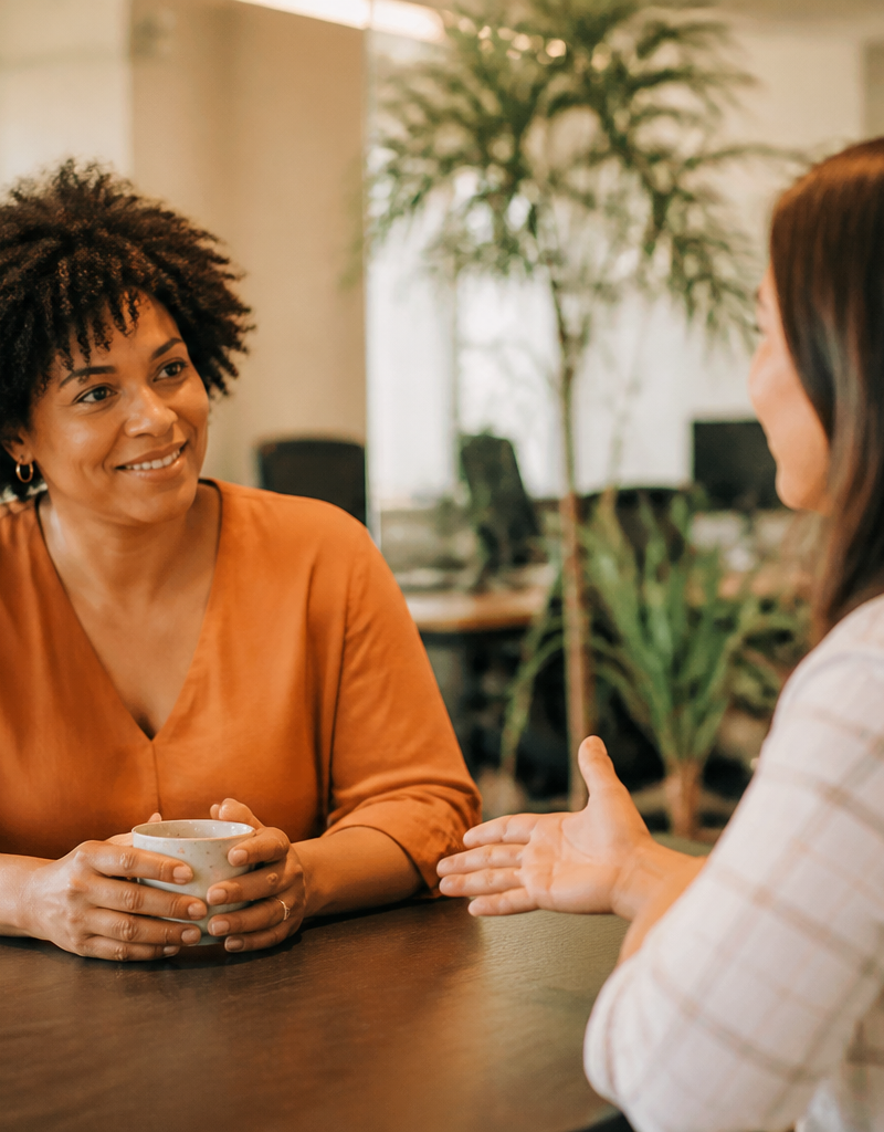 An HR lead and an employee having an open conversation at a desk in a bright UK office.