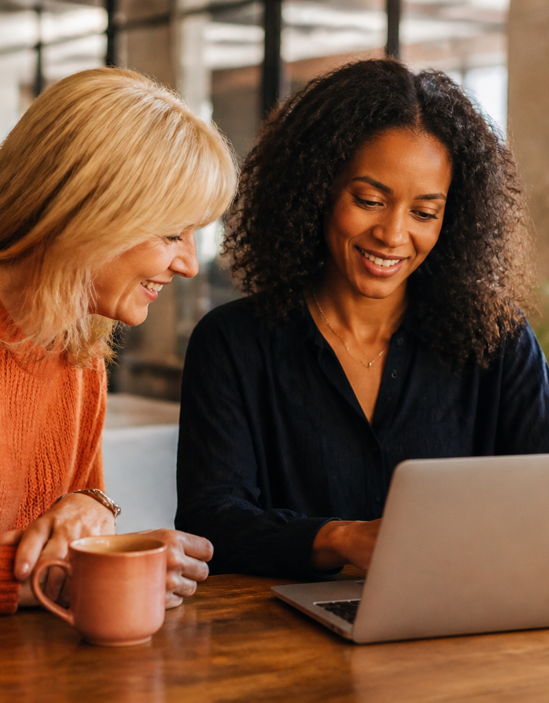 An HR manager and an employee reviewing benefit options on a laptop in a bright office.