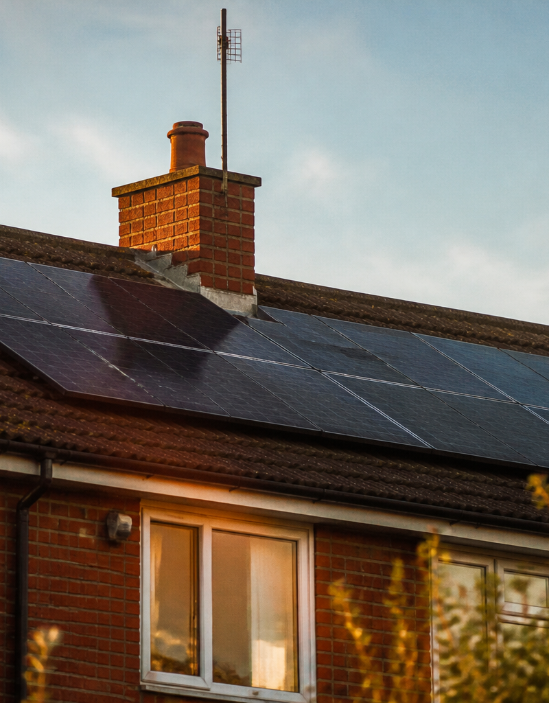 Monocrystalline solar panels installed on a tiled UK house roof near a brick chimney.